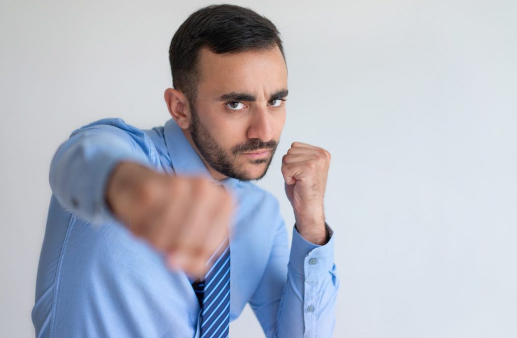 Aggressive young bearded businessman punching camera. Serious handsome man boxing against white background. Challenge concept